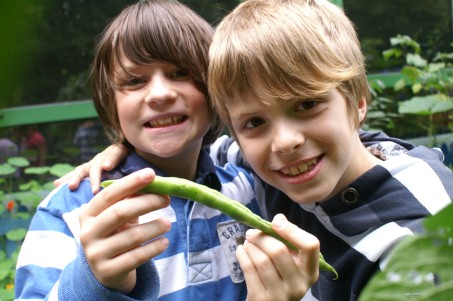 Zwei Jungen präsentieren stolz eine selbstgezogene Bohne aus dem Schulgarten.